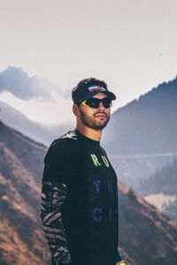 Young man wearing sunglasses standing on mountain against sky