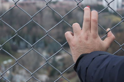 Cropped hand of man on chainlink fence