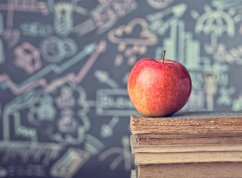 Close-up of apple on books against blackboard