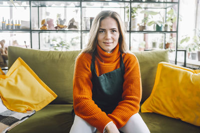 Smiling botanist sitting on sofa in plant store