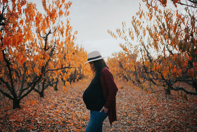 Pregnant woman standing amidst trees against sky during autumn