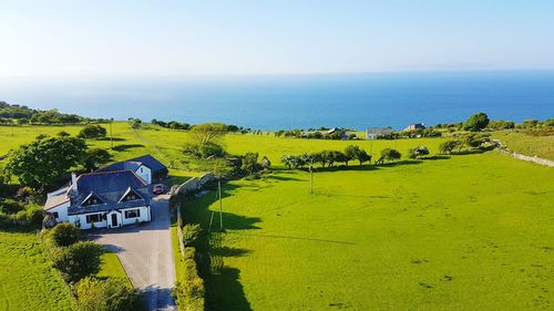 Houses on grassy field by sea against clear sky