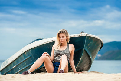 Young woman sitting on beach against sky