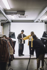 Male fashion designer taking measurement of model during photo shoot at studio