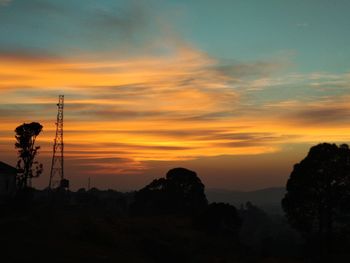 Silhouette trees and electricity pylon against sky during sunset