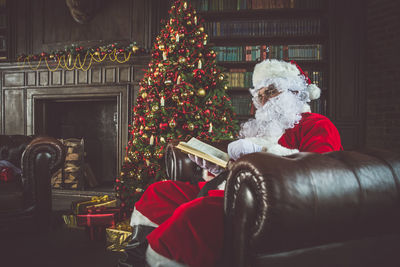Man wearing santa claus costume reading book on sofa at home