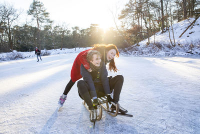 Cheerful couple enjoying sledding and ice-skating on frozen lake