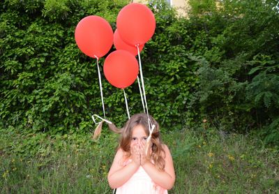 Portrait of girl with balloons standing against trees