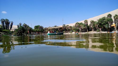 People on riverbank against clear blue sky