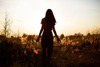 Rear view of silhouette woman standing on field against sky