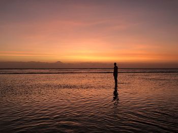 Silhouette man standing in sea against sky during sunset