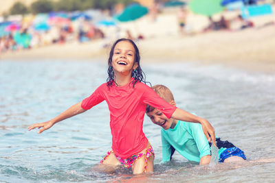 Happy kids at beach playing in sea during summer vacation