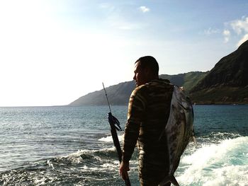 Rear view of man with fish by sea against sky