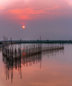 Wooden posts in sea against sky during sunset