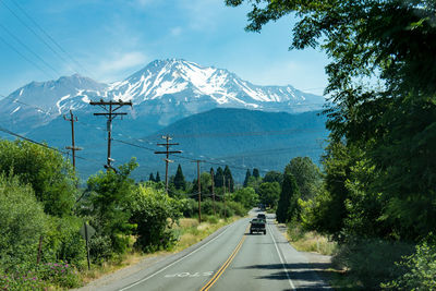 Road amidst trees and mountains against sky