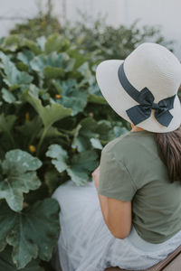 Young girl wearing a sunhat sitting in front of a garden during summer