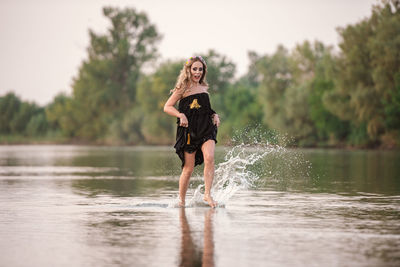 Woman standing by lake against trees