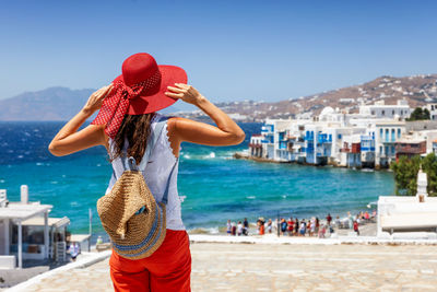 Rear view of woman standing against beach and buildings