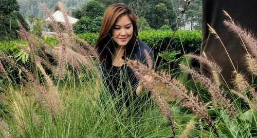 Smiling young woman standing on field against trees