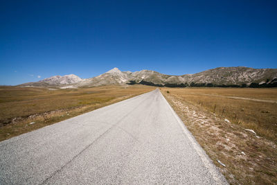 Street leading towards mountains against clear blue sky