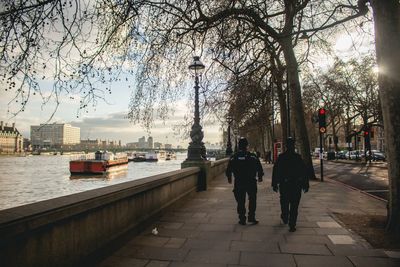 Rear view of police officers walking by river on sunny day