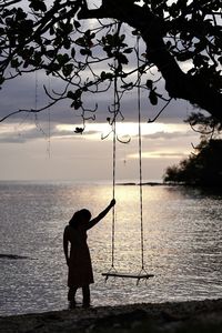 Rear view of man standing at beach against sky during sunset