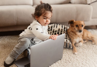 Cute boy holding laptop while sitting with dog at home