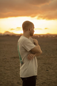 Side view of man standing at beach against sky during sunset