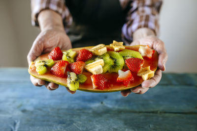 Close-up of man's hands with half papaya with pieces of banana, kiwi and strawberries