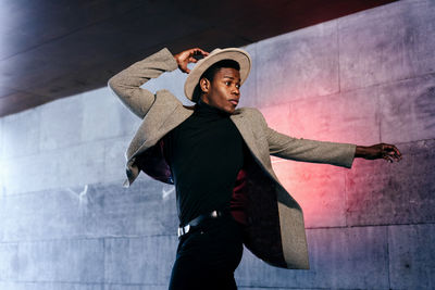 Young man looking away while standing against wall