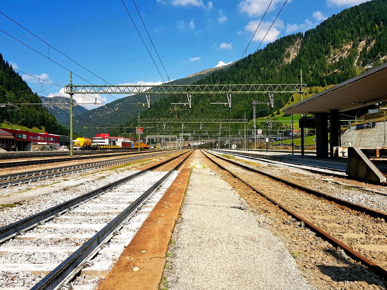 rail transportation, transportation, track, railroad track, mountain, sky, mode of transportation, nature, public transportation, cable, train, built structure, no people, architecture, day, railroad station, electricity, railroad station platform, train - vehicle, travel, outdoors, diminishing perspective, power supply, station