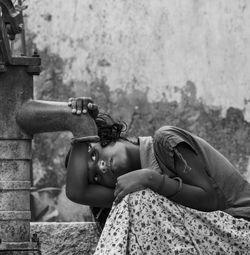 Girl trying to drink water from hand pump against wall