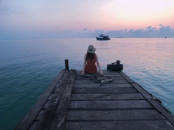 Rear view of woman sitting on pier over sea during sunset