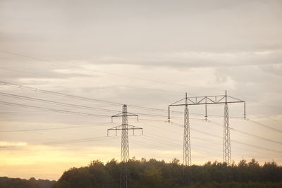 Low angle view of electricity pylons against evening sky