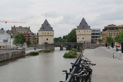 Bridge over river by buildings in city against sky