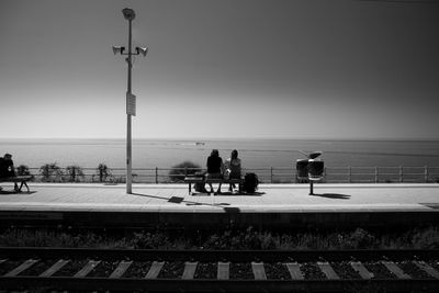People on railroad track by sea against clear sky