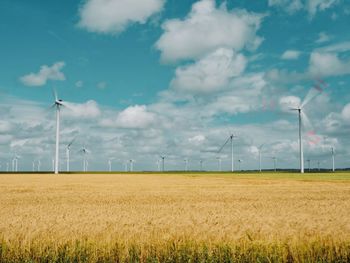 Wind turbines on field against sky