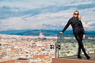 Young woman wearing warm clothing while standing on balcony against cityscape