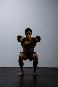 Portrait of shirtless muscular man exercising against wall