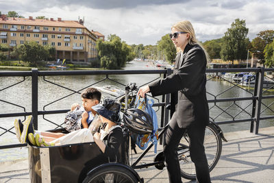 Mother pushing bicycle with children in carriage