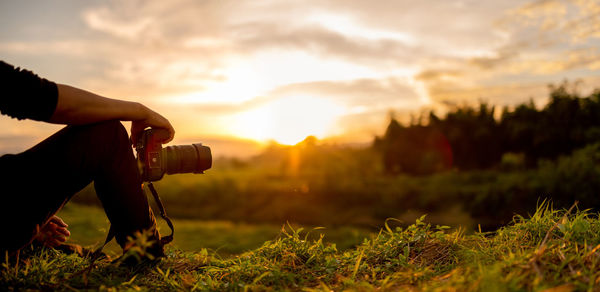 Person photographing on field against sky during sunset