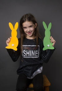 Portrait of smiling girl holding paper eater bunny against gray background