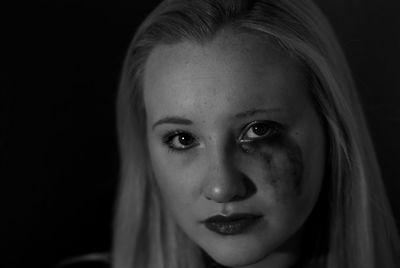 Close-up portrait of young woman with smudged eyeliner against black background