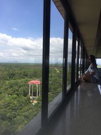 Man sitting by window against sky