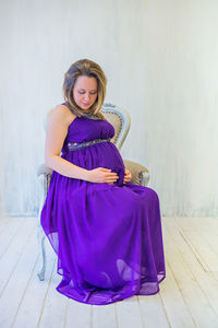 Pregnant woman sitting on chair against wall