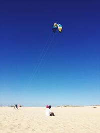 People paragliding on beach against clear blue sky