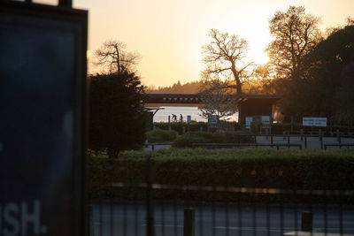 Building by trees on field against sky during sunset