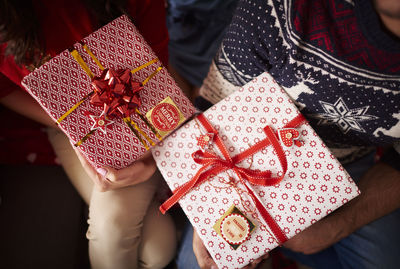 Midsection of people holding christmas presents while sitting at home