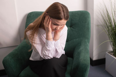 A young girl in a white shirt is sitting in a chair in the psychologist's office 