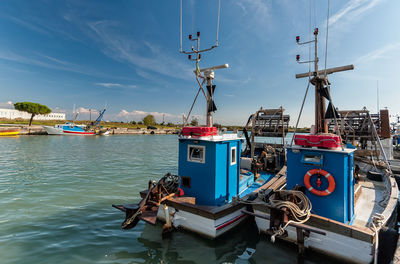 Fishing boats moored at harbor against sky